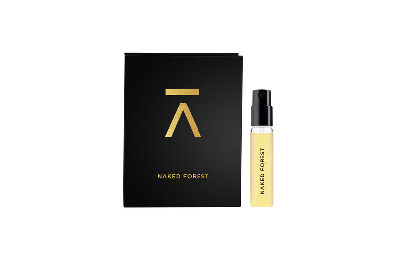 Studio photograph of ‘Naked Forest’ perfume bottle by Azman Perfumes in collaboration with Prin Lomros, against a white background. The perfume features a green, veggie and mysterious aesthetic with elements of iris, Sandelwood, mango etc. Picture depicts nature in a very subtle way showing bottle resting on natural black stone and dead dry leaf leaning to the bottle. 